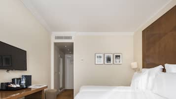 A hotel room with a bed, a desk with a flat-screen TV, a coffee maker, and a water bottle.