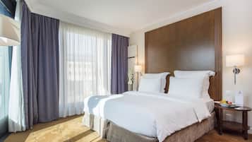 Una habitación de hotel con una cama grande, una mesita de noche, una lámpara y un ventanal con cortinas.
