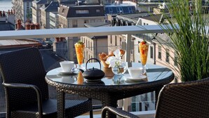 A balcony with wicker chairs and a table set with a teapot, cups, and a fruit drink. - Warwick Geneva (Geneva)