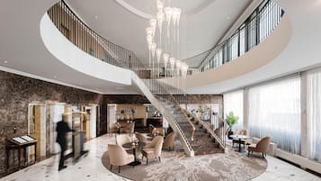 Un hall d’entrée spacieux, doté d’un sol en marbre, d’un espace salon central et d’un grand escalier menant à un niveau supérieur.