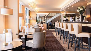 A hotel lobby with round tables, bar stools, a staircase, and a bar area. - Warwick Geneva (Geneva)