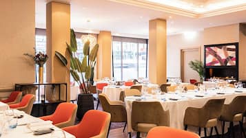 Un espace de restauration d’hôtel avec de nombreuses tables dressées pour les clients, de grandes fenêtres et un aménagement intérieur moderne.