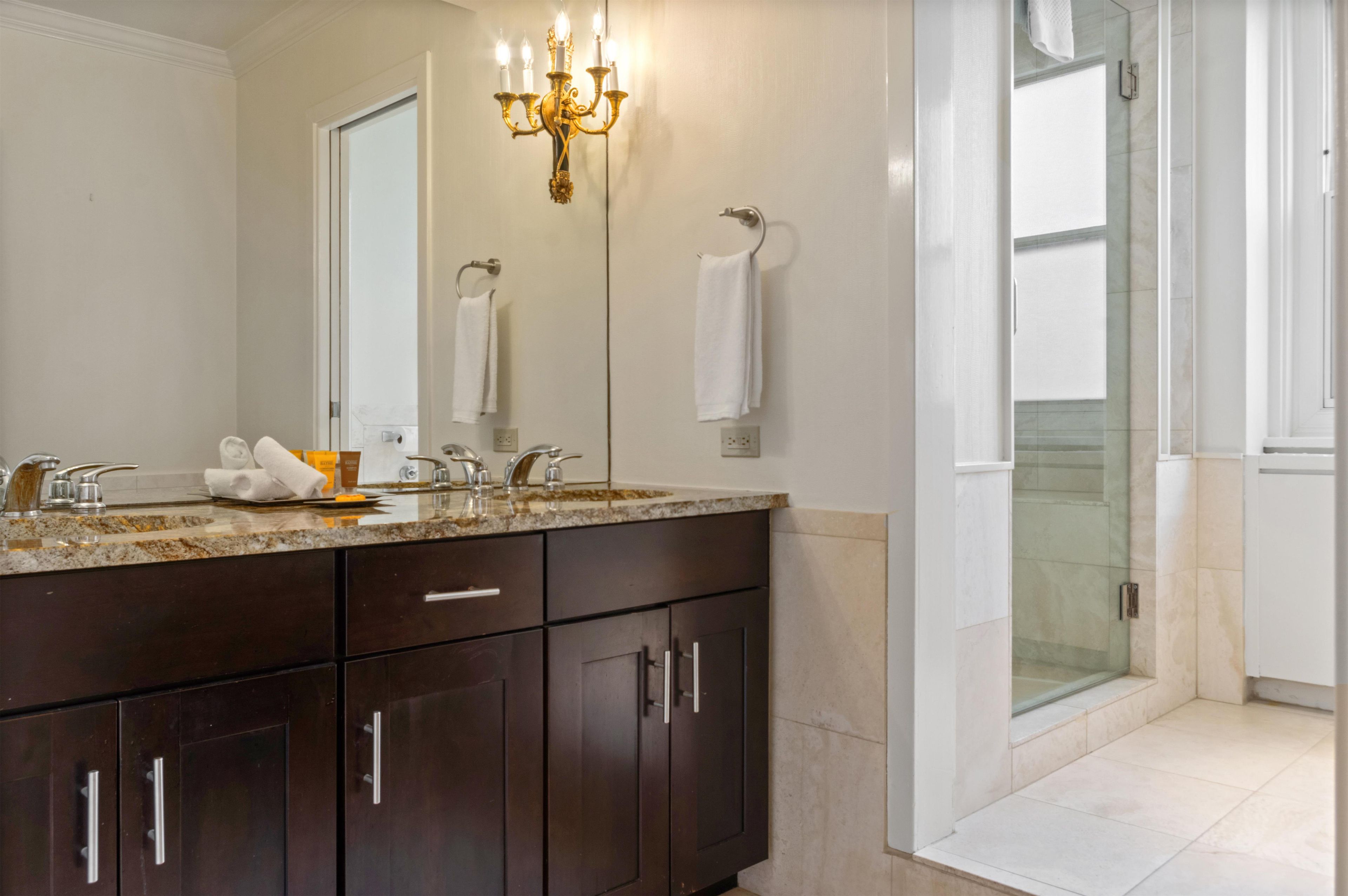 A modern bathroom with a dark wood vanity, a large mirror, and a glass shower enclosure.