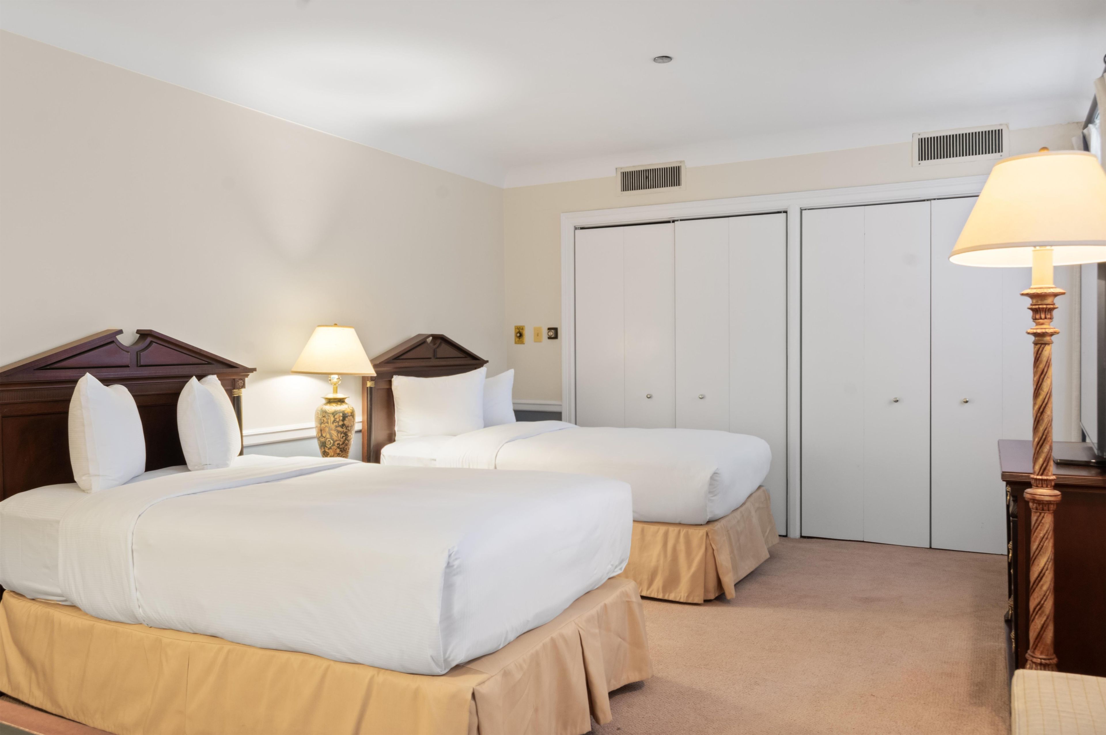 Ein Hotelzimmer mit zwei Betten, einem Kleiderschrank, einem Nachttisch mit Lampe und Teppichboden.