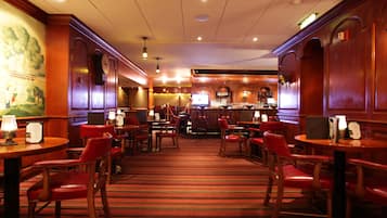 A hotel lobby with wooden paneling, red leather chairs, a carpeted floor, and a bar area with a television.