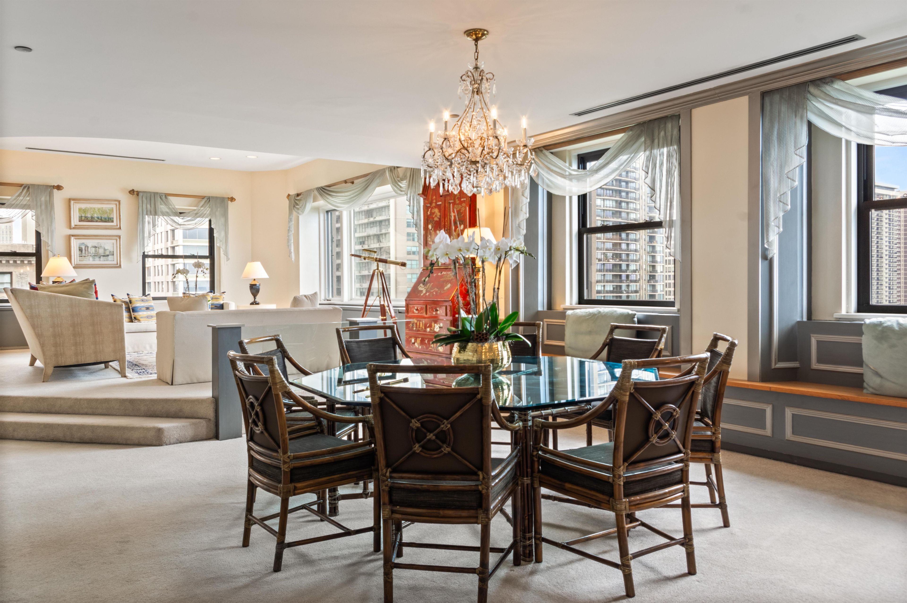 A spacious dining area with a round table, wicker chairs, and a chandelier.