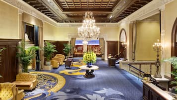A grand lobby with a chandelier, plush seating, and a patterned carpet.