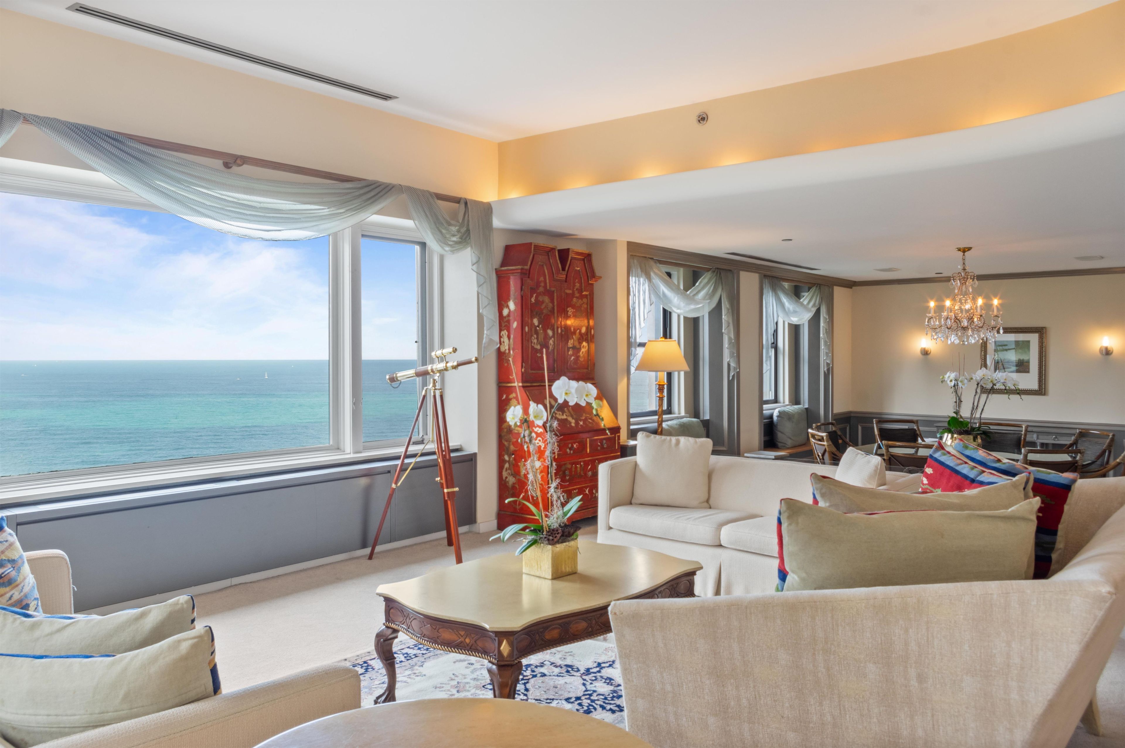 A spacious living room with a large window overlooking the sea, a chandelier, and a dining area with a view.