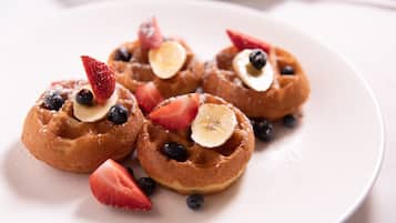 Quatre waffles petits coberts amb fresons, gerros i làmines de plàtan, presentats sobre un plat blanc.