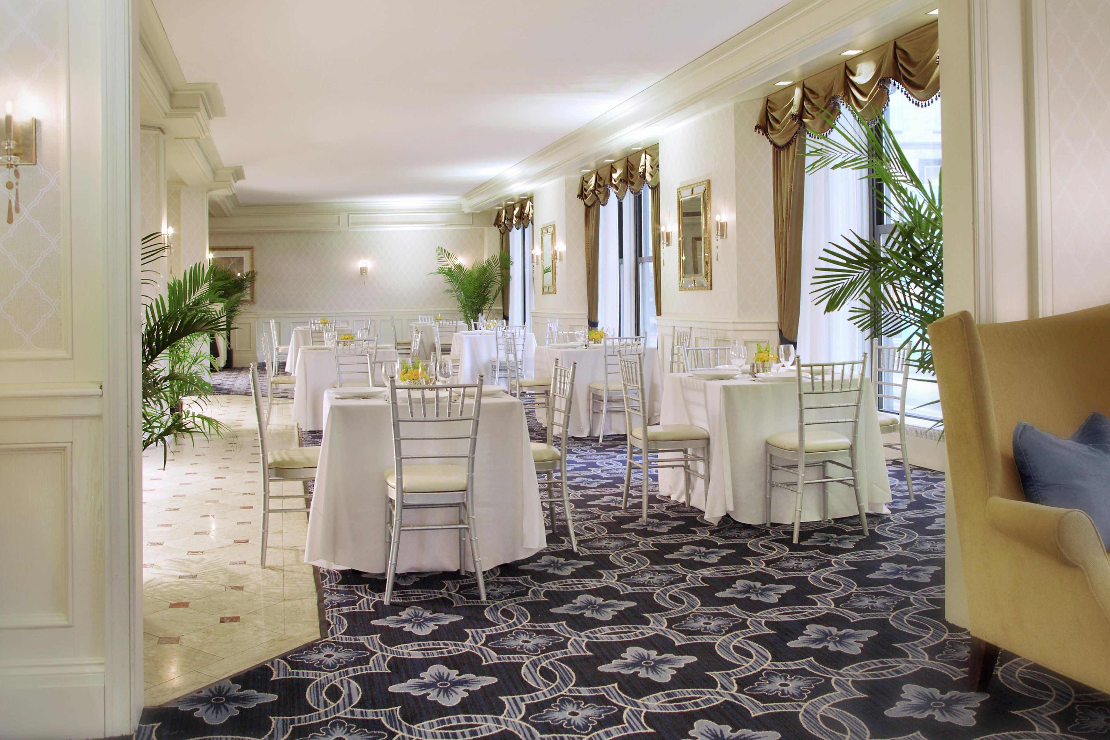 A formal dining room with multiple round tables, white tablecloths, and chairs.