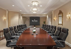 A conference room with a long table, black leather chairs, chandeliers, and a screen displaying "The Drake Real Chicago". - The Drake (Chicago)