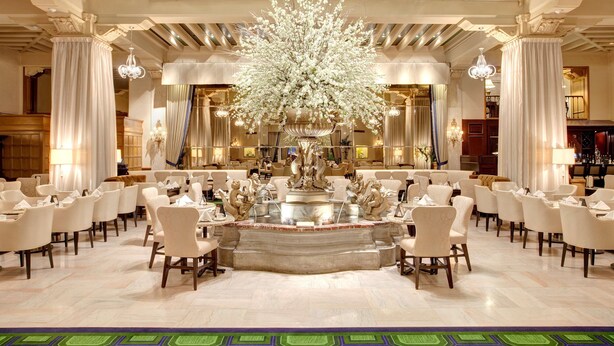 A spacious hotel lobby with a central fountain, elegant chandeliers, and a high ceiling with skylights. - The Drake (Chicago)