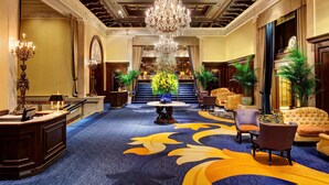 A grand lobby with a chandelier, a reception desk, and a seating area with sofas and chairs. - The Drake (Chicago)