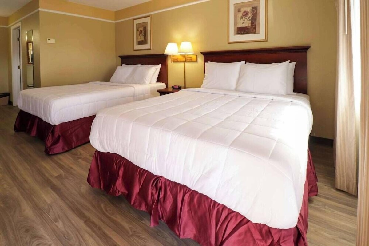 A hotel room with two beds, a wooden floor, a wall-mounted lamp, and a door.