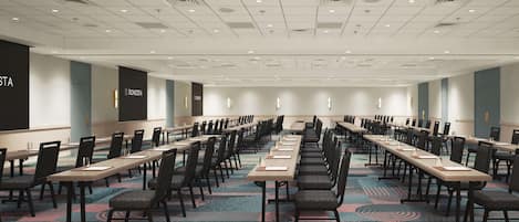 A conference room with long tables and chairs, a patterned carpet, and a white ceiling with recessed lighting.