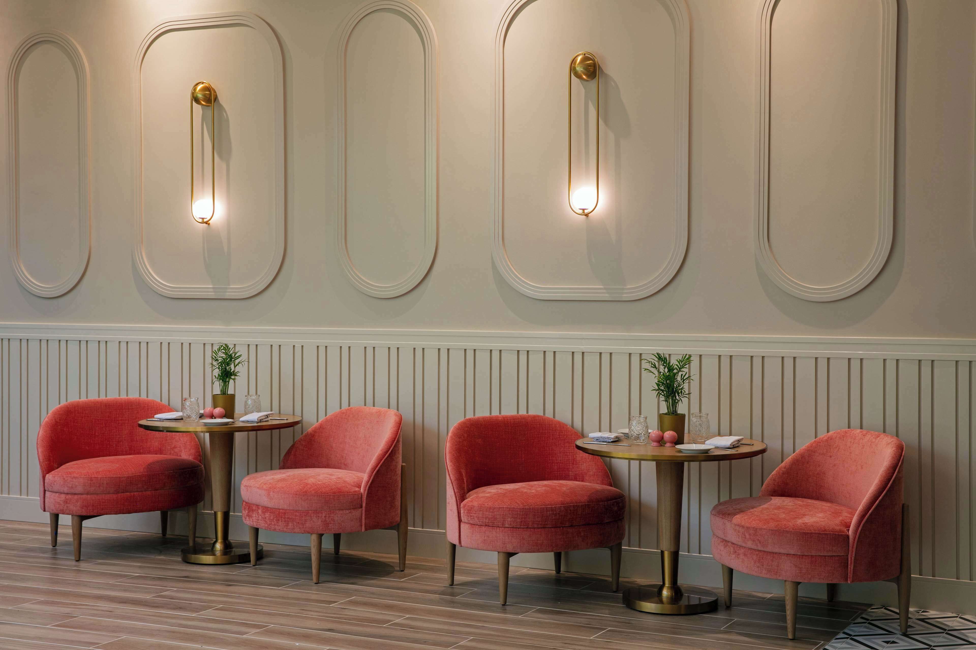 Una habitación con cuatro sillas tapizadas de rojo alrededor de una mesa redonda, una pared con lámparas decorativas y suelo de madera.