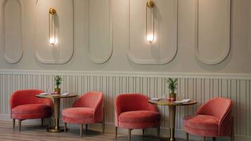 Una habitación con cuatro sillas tapizadas de rojo alrededor de una mesa redonda, una pared con lámparas decorativas y suelo de madera.