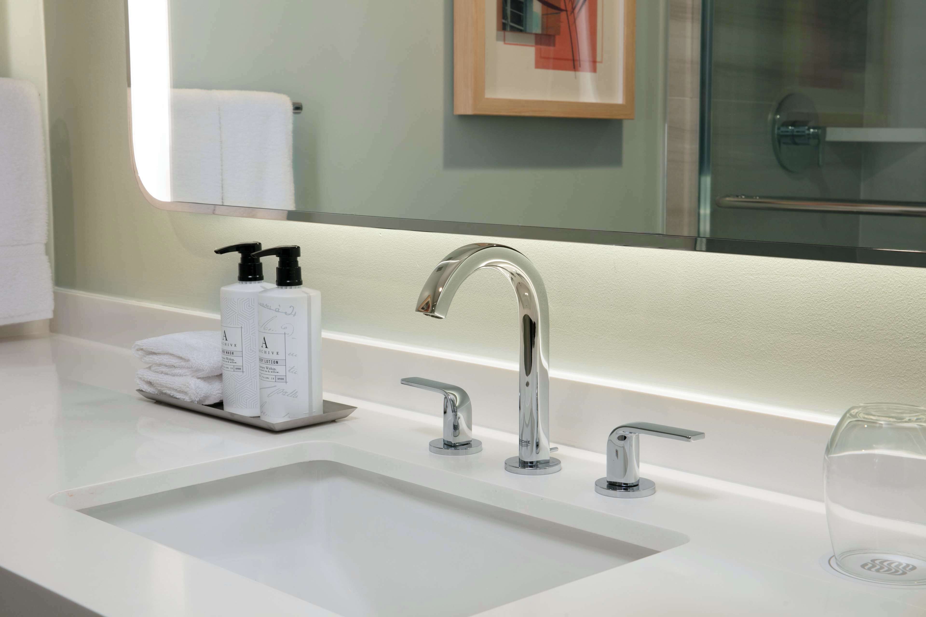 Un baño moderno con un lavabo blanco, dos grifos y un espejo grande.