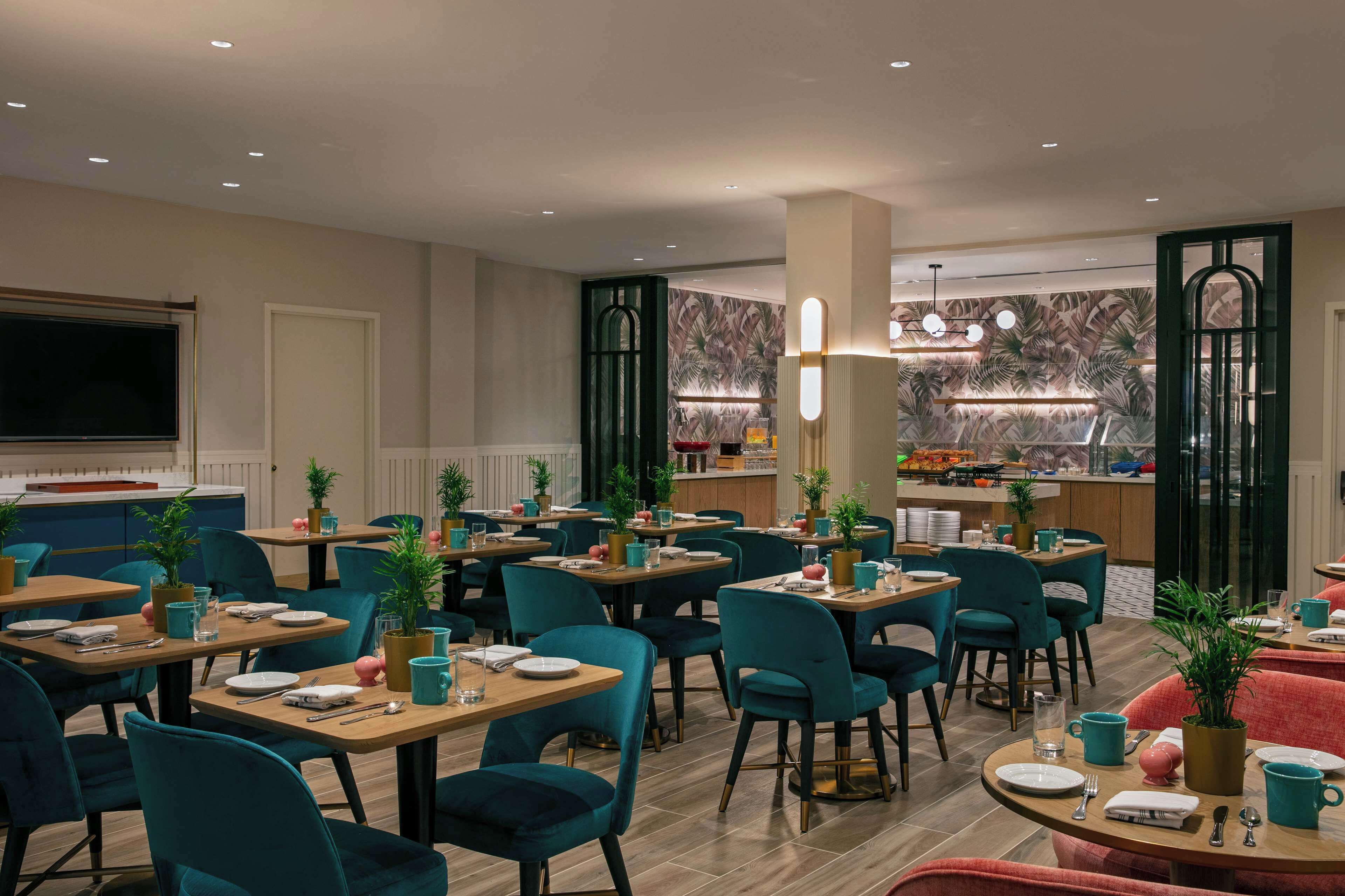 A restaurant with multiple tables and chairs, a bar area, and potted plants.