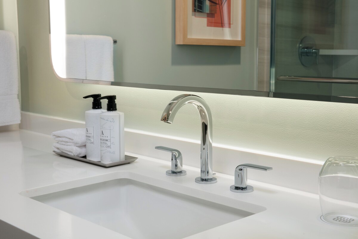 A modern bathroom with a white sink, two faucets, and a glass container.