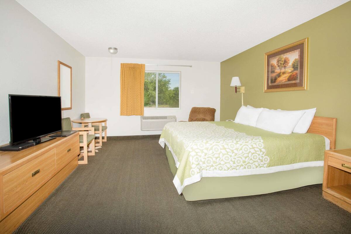 Une chambre d’hôtel comprenant un lit, une télévision, un bureau, une chaise, une fenêtre avec des rideaux et un tableau au mur.