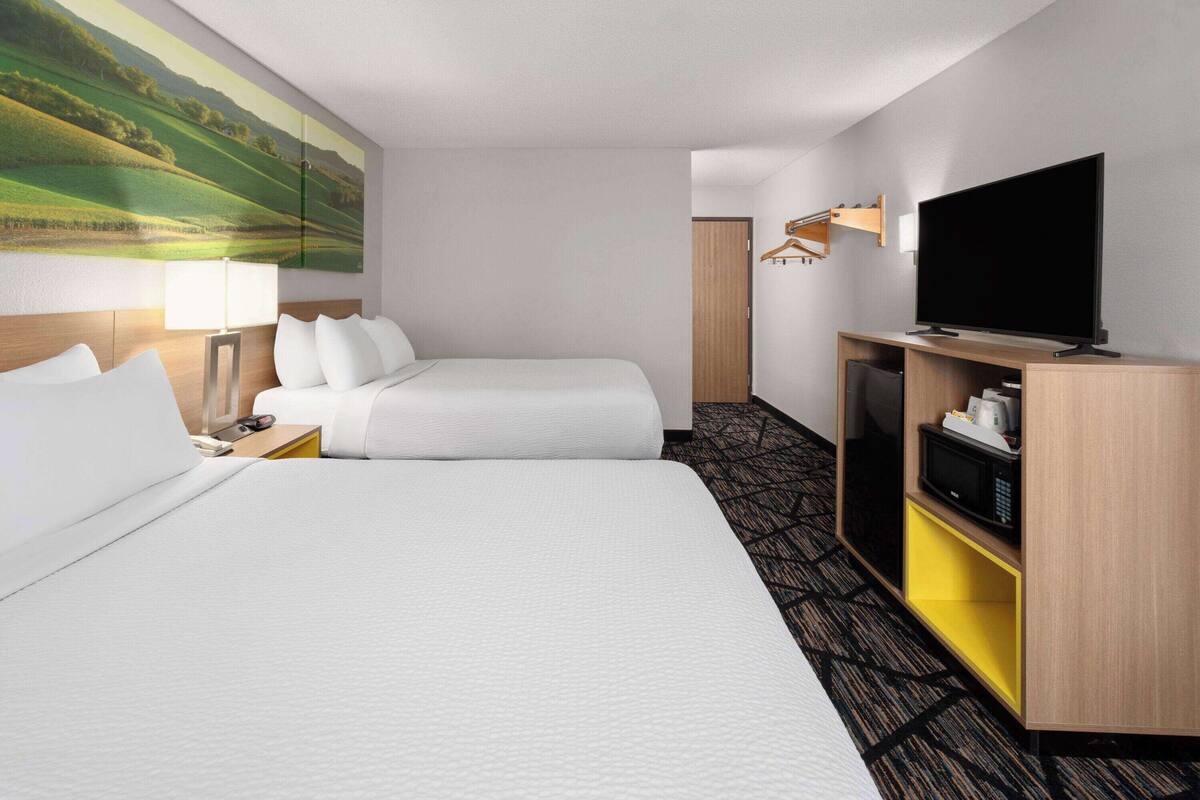 Une chambre d’hôtel avec deux lits, un téléviseur à écran plat, un bureau avec une lampe et un tableau au mur.