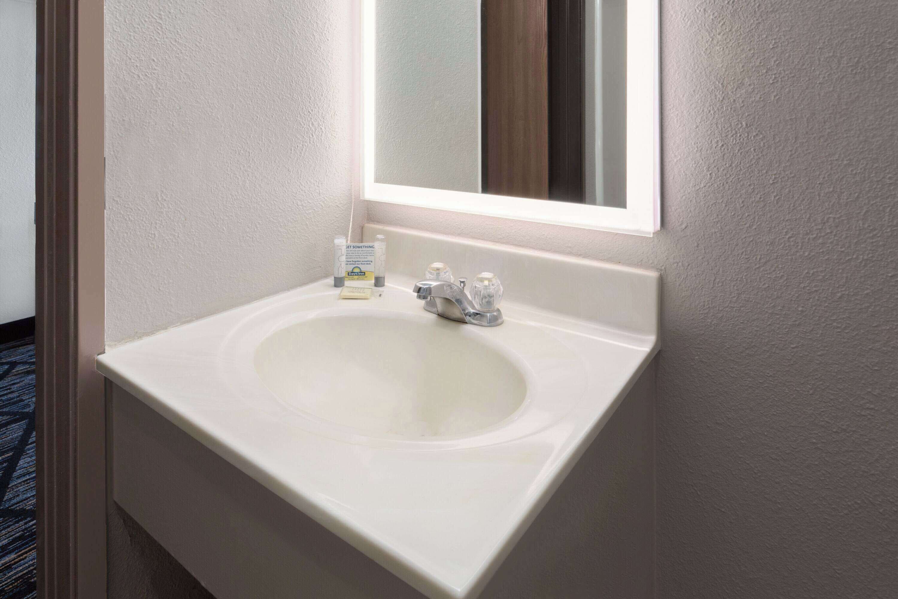 Ein weißes Waschbecken mit Spiegel darüber, einem Seifenspender und einer Handseifenflasche.