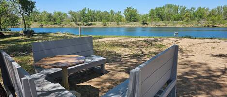 Un conjunto de banco y mesa de madera cerca de un lago, rodeado de árboles y follaje.