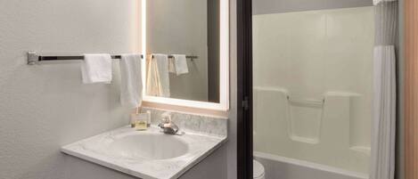 Un baño con lavamanos blanco, espejo y zona de ducha.