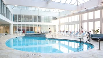 Una piscina interior con techos de vidrio transparente, sillas de descanso y un área de estar.