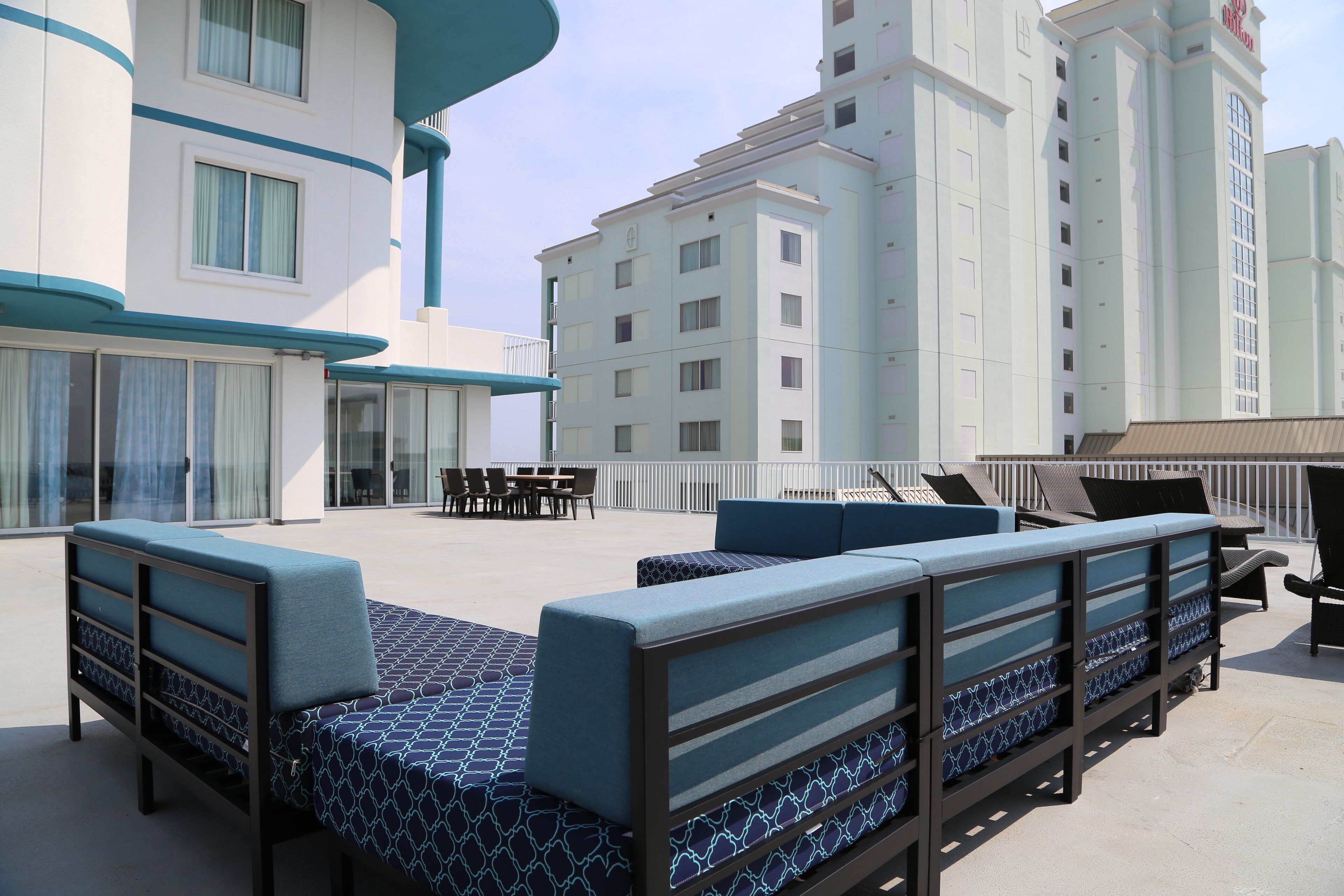 A rooftop lounge area with seating and tables, surrounded by high-rise buildings.