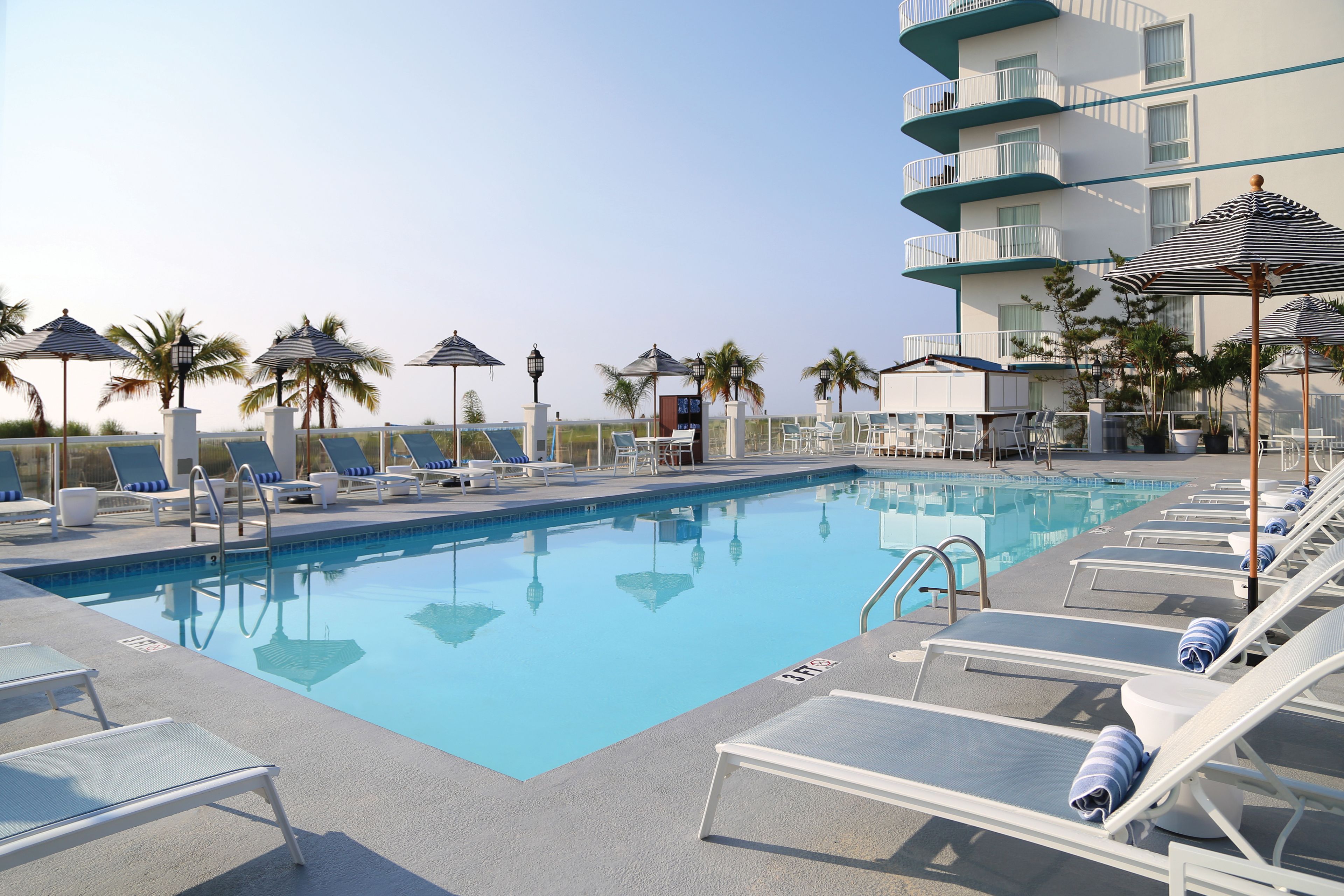 A pool area with lounge chairs, umbrellas, and a building with balconies.