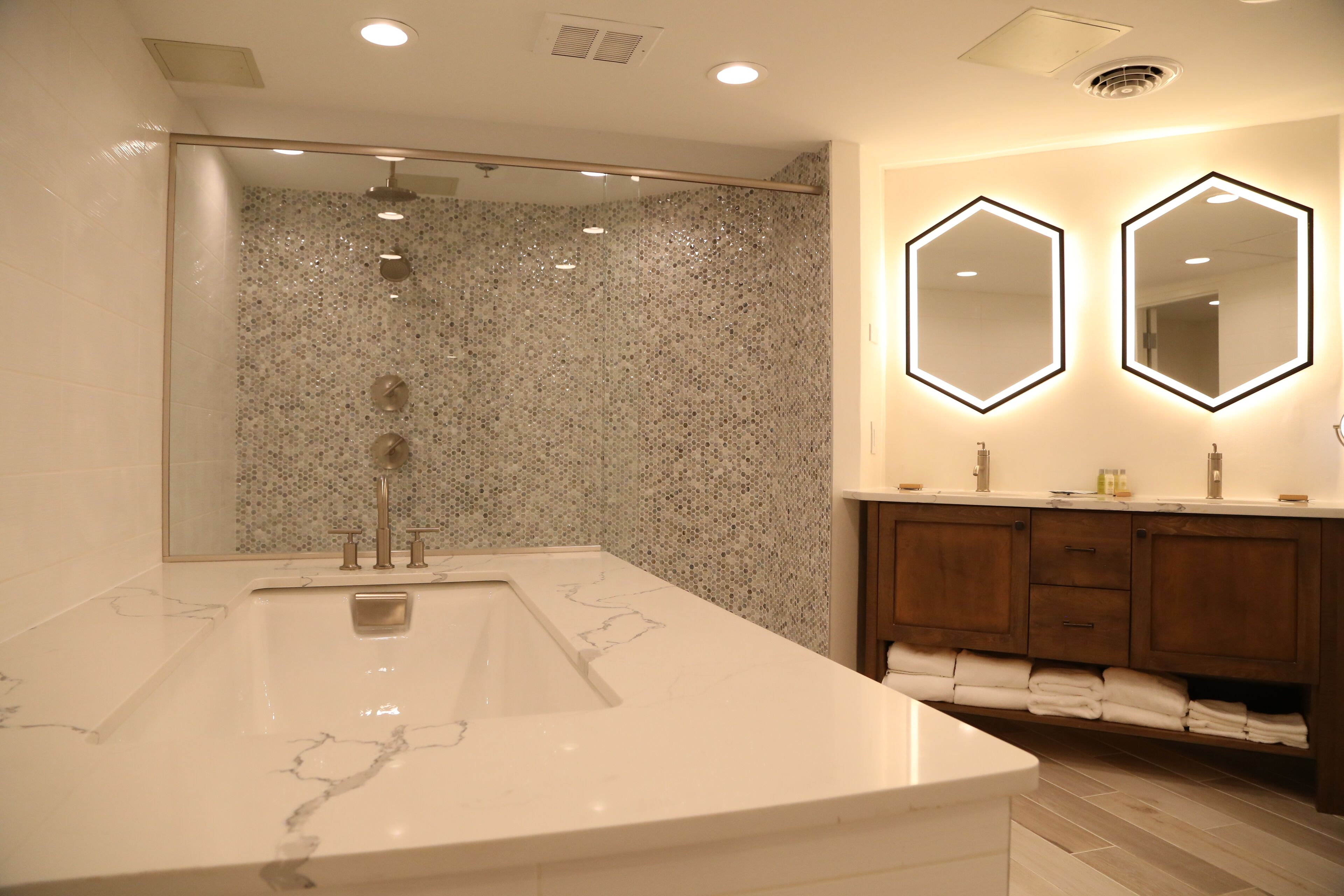A modern bathroom with a large marble sink, a glass-enclosed shower, and wooden cabinets.