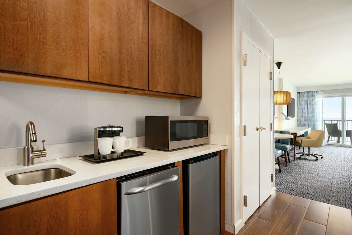 A compact kitchen with a sink, microwave, and dishwasher, wooden cabinets, and a view into a dining area with a table and chairs.