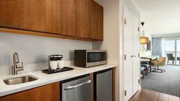 Cocina compacta con lavamanos, microondas y lavavajillas, armarios de madera y vista hacia un comedor con mesa y sillas.