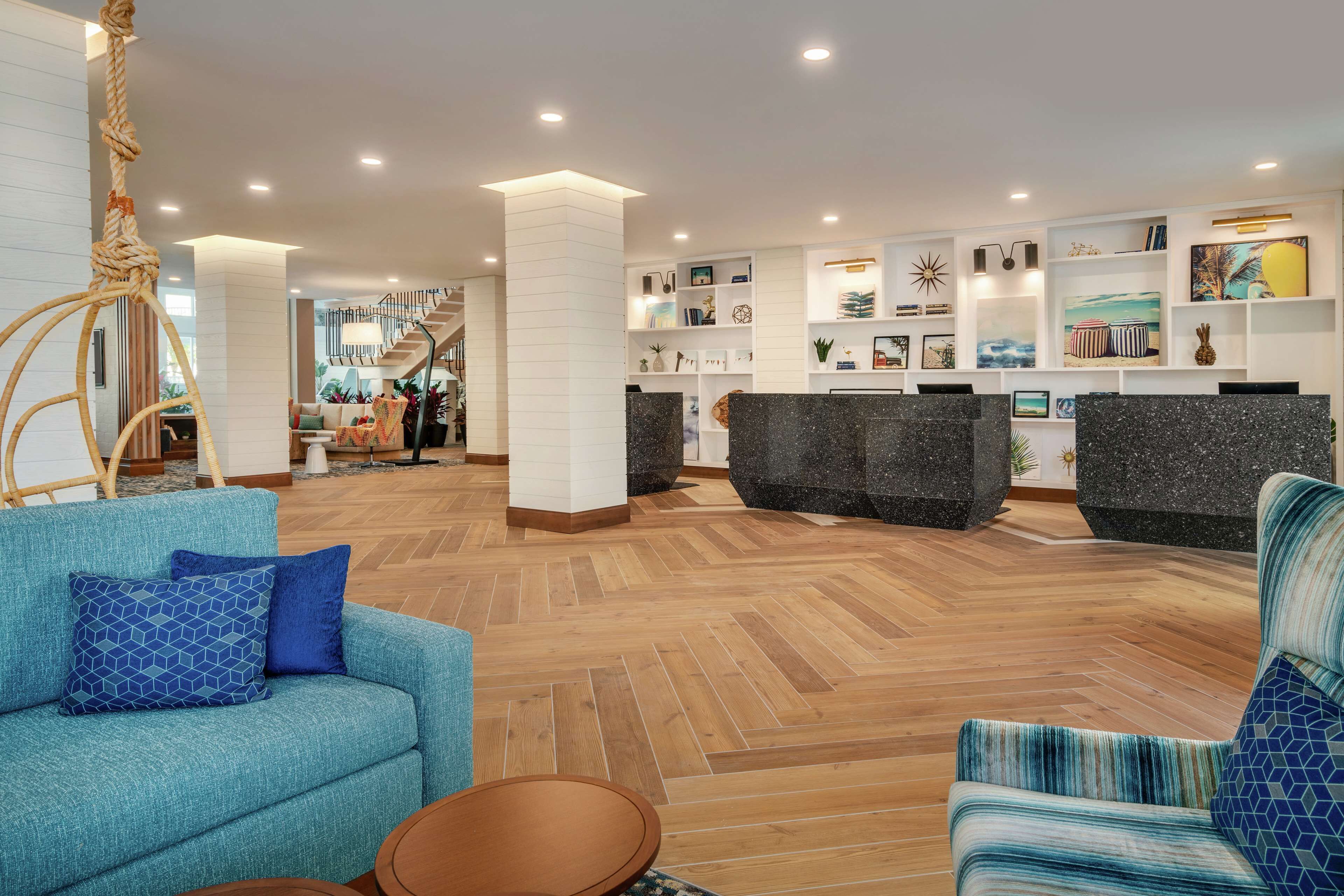 A modern lobby with a wooden herringbone floor, a reception desk, and a staircase leading to upper floors.