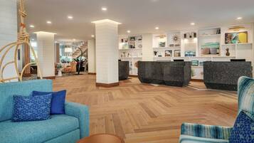 A modern lobby with a wooden herringbone floor, a reception desk, and a staircase leading to upper floors.