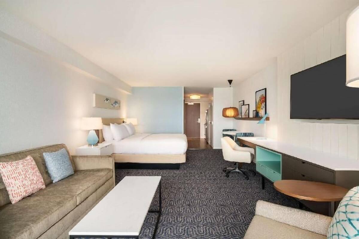 A hotel room with a bed, a desk, a sofa, a TV, and a lamp.