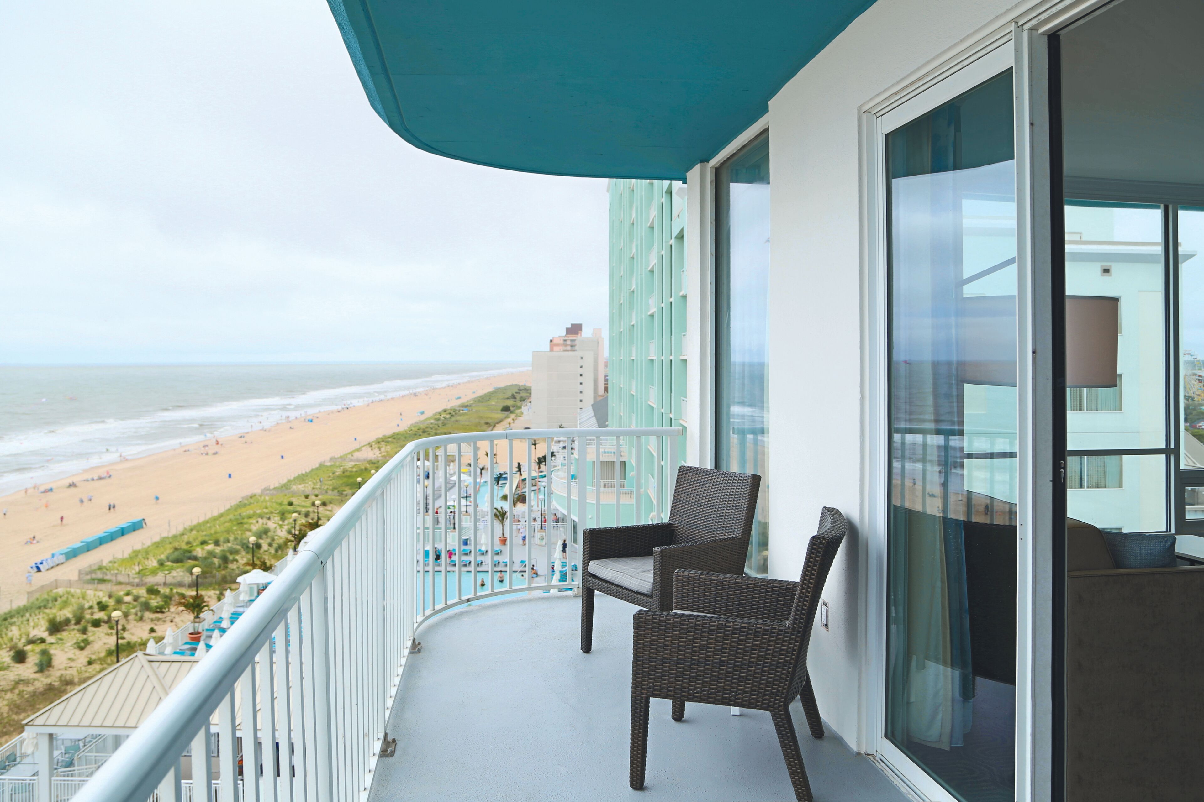 A balcony with wicker chairs, a view of the beach, and a pool area.