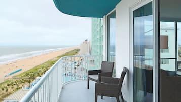 A balcony with wicker chairs, a view of the beach, and a pool area.