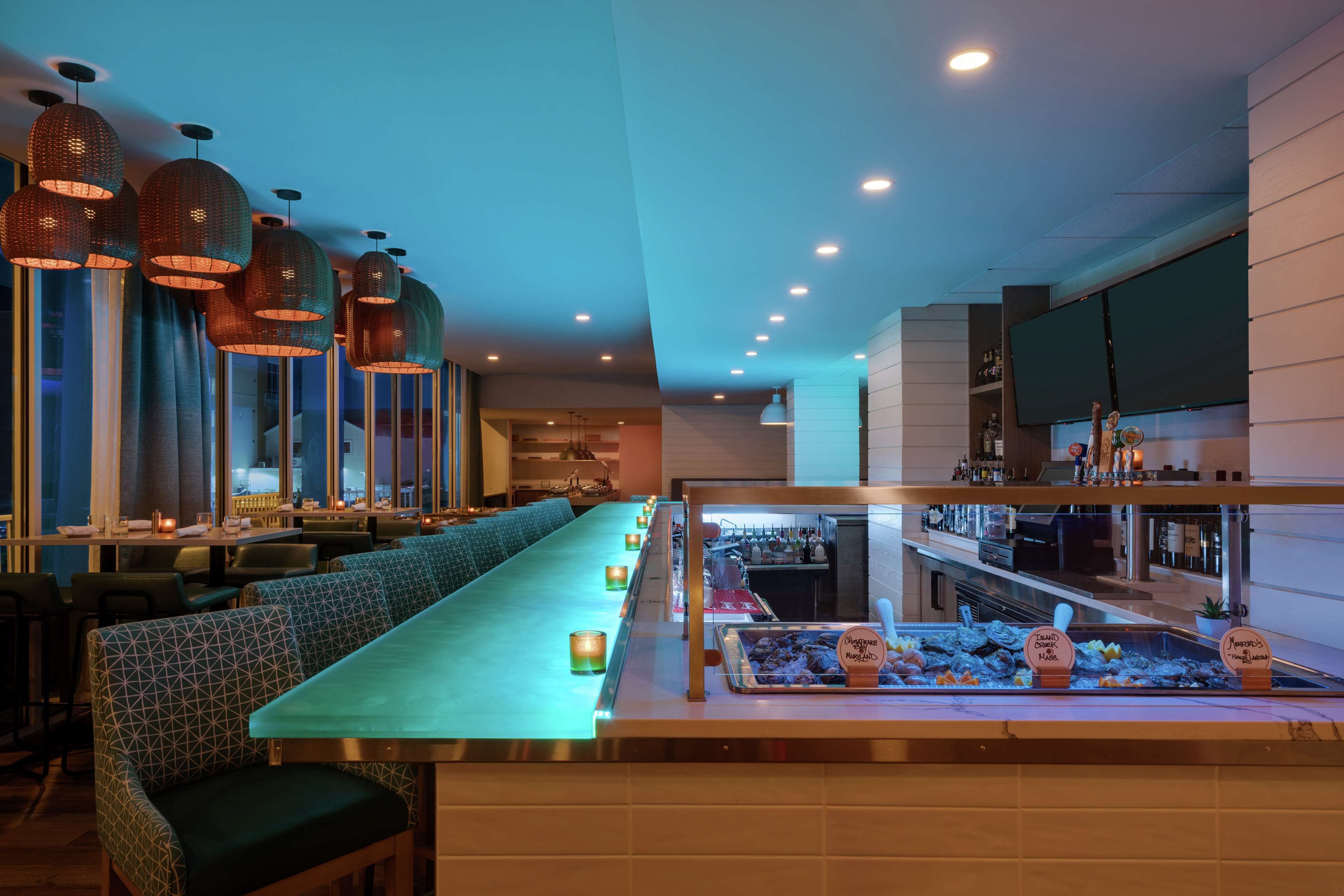 A restaurant with a long counter, patterned seating, hanging pendant lights, and a dessert display.