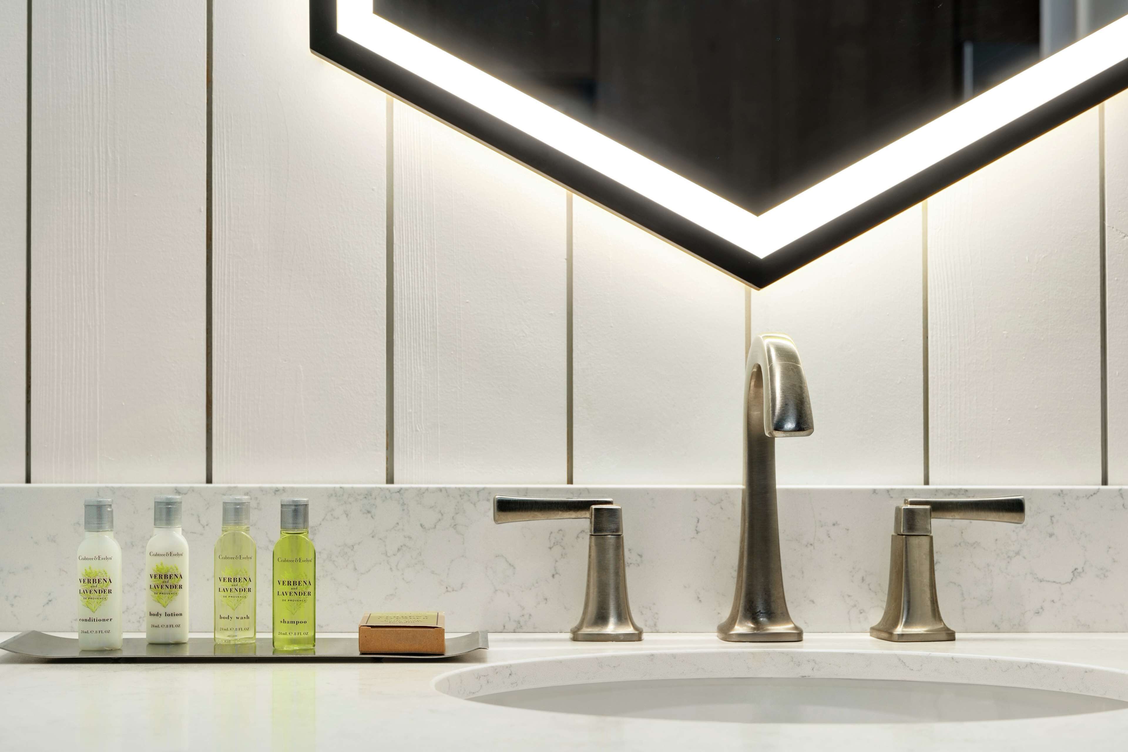 A bathroom with a modern design, featuring a large mirror, two sinks, and a vanity area with toiletries.
