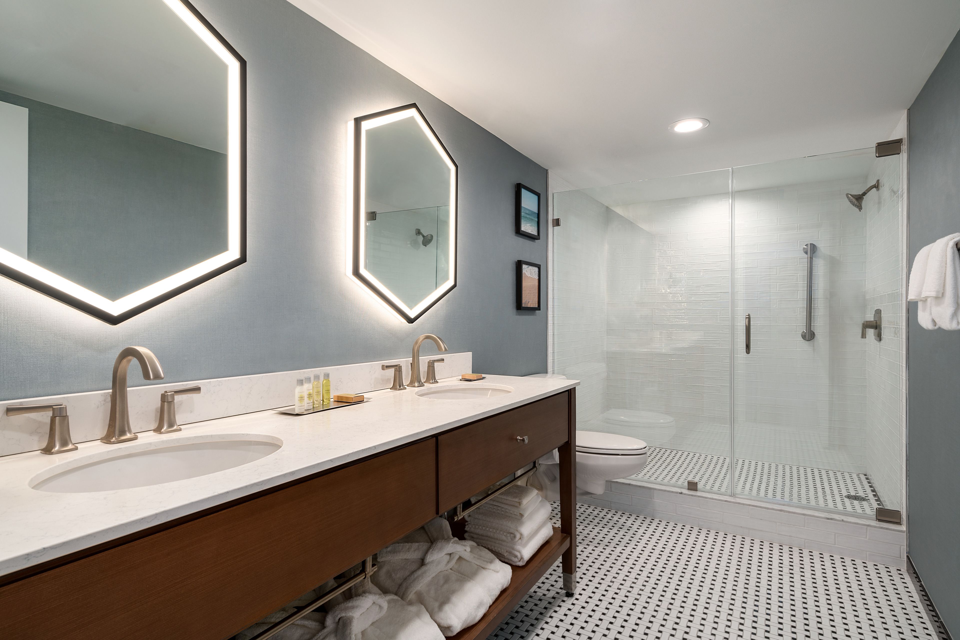 A modern bathroom with two sinks, a large mirror, and a glass-enclosed shower.