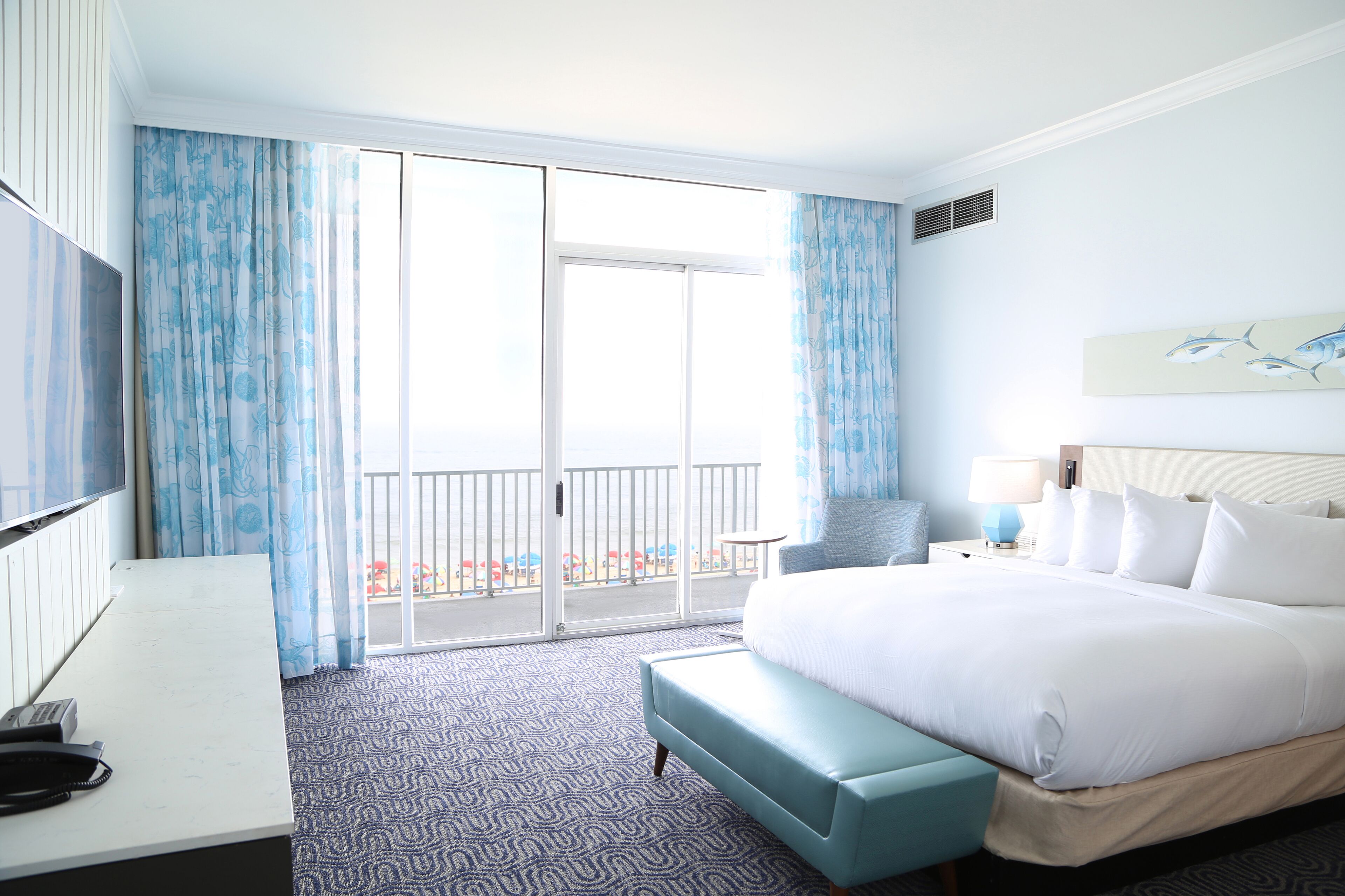 A hotel room with a large bed, a desk with a telephone, a chair, a lamp, and a painting on the wall.