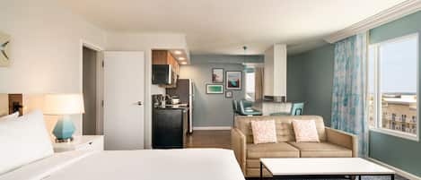 Habitación de hotel con cama, escritorio, sofá, kitchenette y vistas a la ciudad.