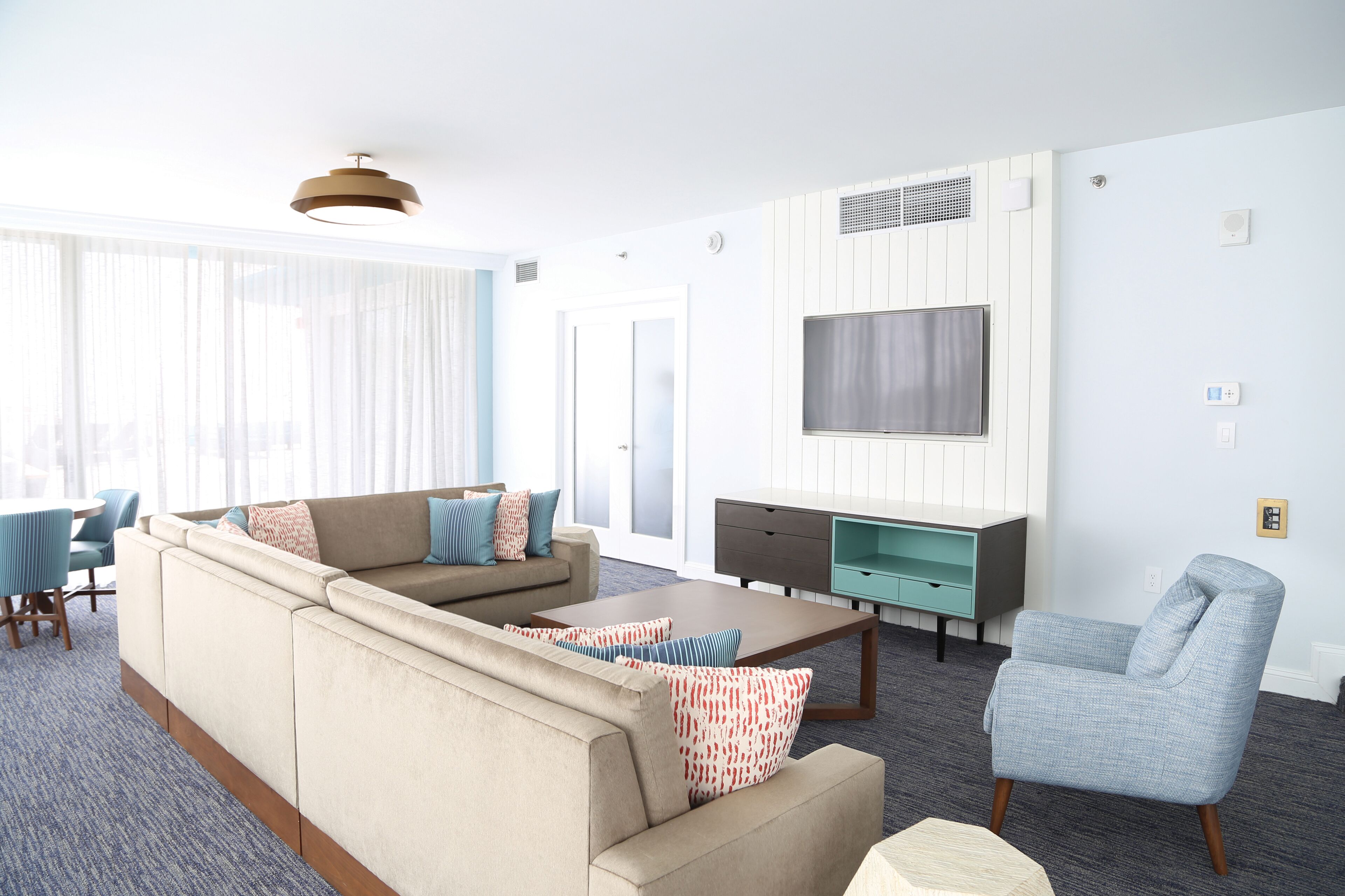 Una sala moderna con sofá, sillón y mesa de centro, un televisor montado en la pared, y un comedor con sillas y mesa.