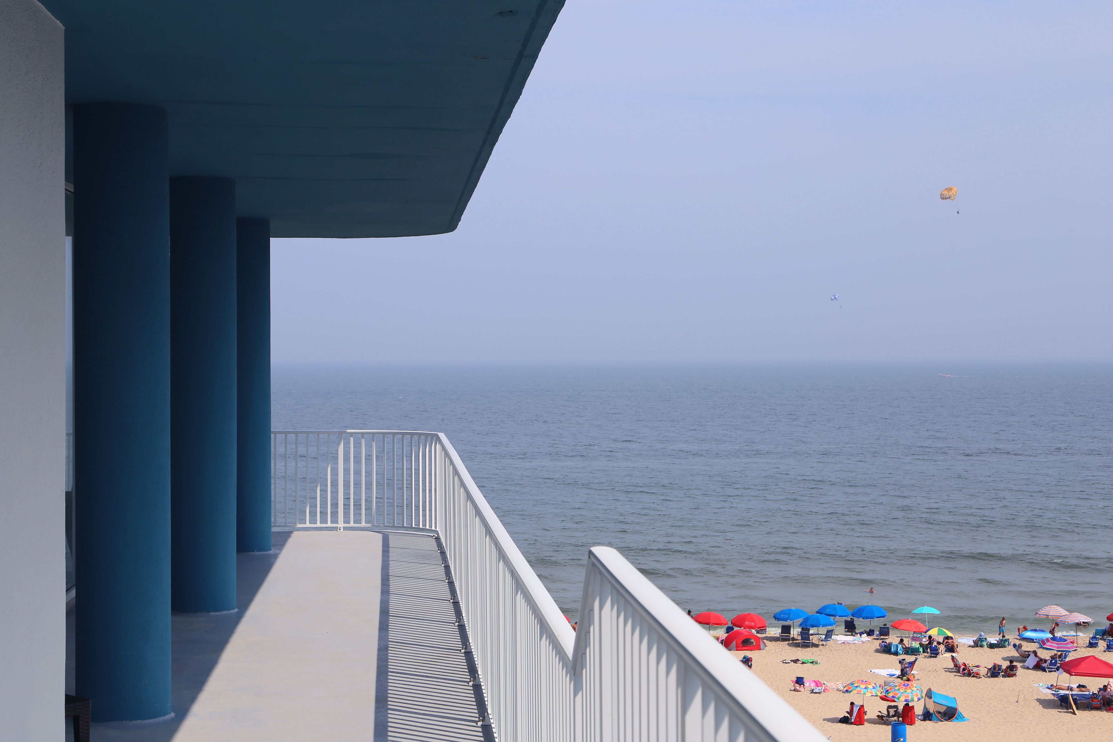 A balcony with blue columns overlooking a beach with umbrellas and people.