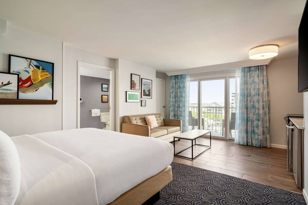 A hotel room with a bed, a sofa, a coffee table, and a balcony with curtains.