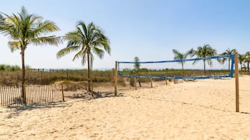 Una red de voleibol de playa con palmeras y una cerca al fondo.