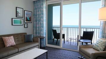 A hotel room with a balcony, a sofa, a small table, and a chair.